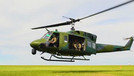 Ein-Bunter-Helikopter-Schwebt-über-Einer-Grasbewachsenen-Ebene-Mit-Uns-Service-Und-Kräften,-Die-Die-Mission-In-Zeitlupe-Bewachen