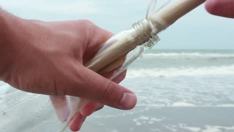 Young-Man-Opening-Message-In-A-Bottle-On-Sand-Beach-1