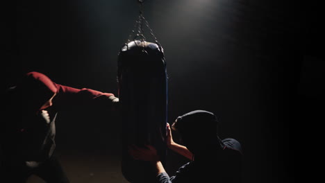 Two-young-fighter-fighters-train-with-a-punching-bag