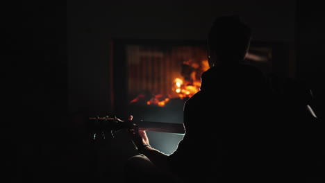A-young-man-plays-the-guitar-by-a-fireplace-1