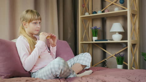 Child-eats-a-sandwich-sits-on-the-bed-and-watches-TV