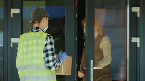 A-courier-wearing-a-mask-and-protective-gloves-delivers-a-parcel