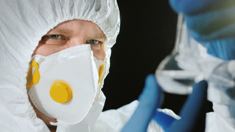 Scientist-in-protective-suit-looks-at-a-test-tube-with-a-transparent-drug