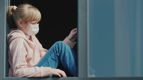 A-Child-In-A-Medical-Mask-Looks-Out-Of-The-Window