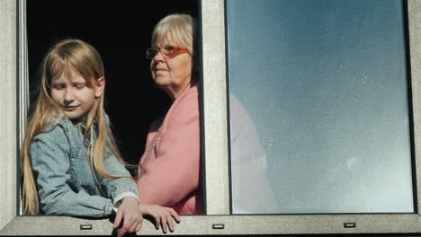 Eine-ältere-Frau-Neben-Dem-Kind-Sitzt-Auf-Der-Fensterbank-Und-Schaut-Aus-Dem-Fenster