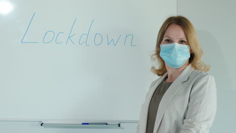 A-Masked-Teacher-Stands-At-The-Board-With-The-Word-Lockdown-Written