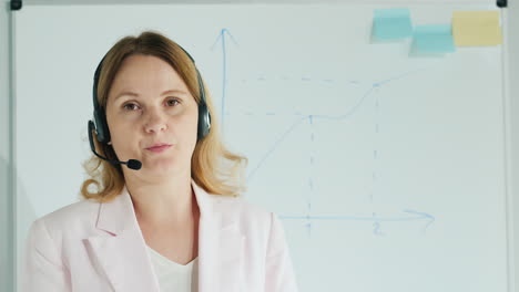 Blogger-In-Headset-Talks-To-The-Camera-Against-The-Background-Of-A-Board-With-Diagrams
