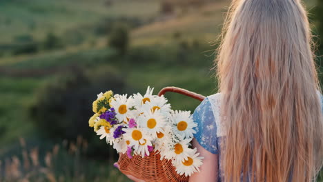 A-child-holds-a-basket-of-flowers-stands-in-a-meadows-and-green-hills-2