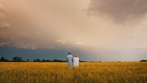 A-Man-And-A-Woman-Stand-In-A-Field-Of-Wheat-Against-A-Stormy-Sky-Where-Lightning-Is-Visible