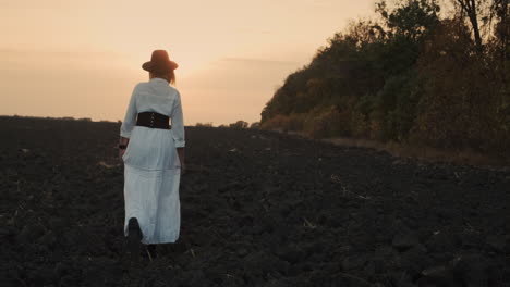 A-woman-in-a-dress-walks-through-a-plowed-field-on-black-soil