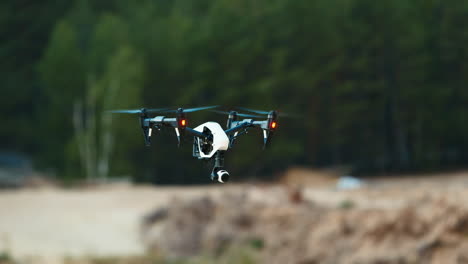 Die-Drohne-Schwebt-In-Der-Luft-Vor-Dem-Hintergrund-Des-Sandigen-Ufers-Und-Des-Waldes