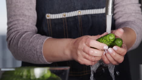 A-woman-in-an-apron-washes-cucumbers-under-a-stream-of-water-from-a-kitchen-tap