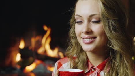 A-young-woman-drinks-tea-by-the-burning-fireplace
