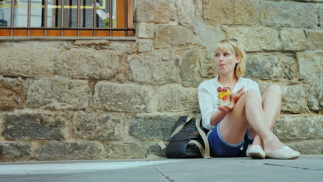 A-tired-tourist-eats-fruit-sits-on-the-sidewalk-in-the-old-part-of-the-city-of-Barcelona