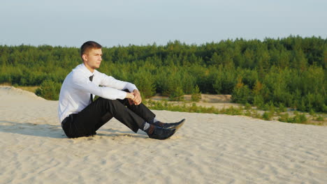 A-young-businessman-in-a-suit-sits-on-the-sand