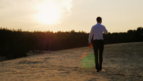 A-businessman-with-a-bottle-of-alcohol-walks-forward-on-the-sand