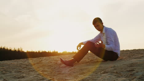 A-young-businessman-holds-sand-in-his-hand-sitting-at-sunset-on-the-beach