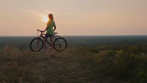 Silueta-De-Una-Mujer-Con-Una-Bicicleta-Admirando-La-Puesta-De-Sol