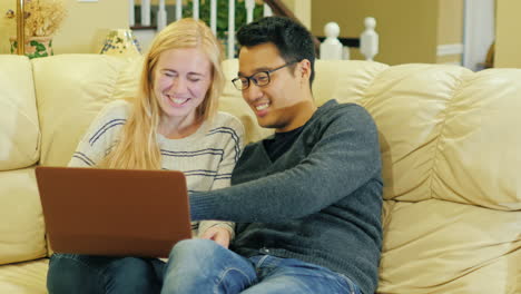 A-Young-Couple-Sitting-On-The-Couch-Using-A-Laptop-1