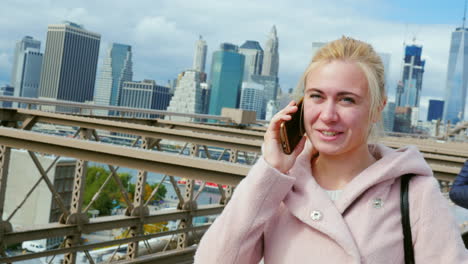 A-Young-Woman-Is-On-The-Phone-Standing-On-The-Brooklyn-Bridge-In-New-York