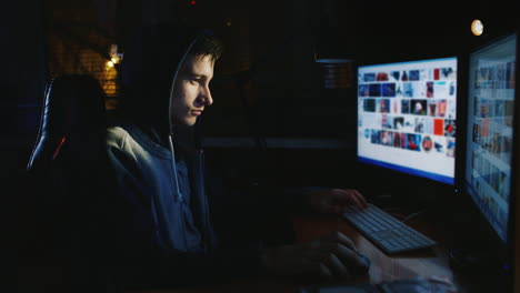 A-Teenager-In-A-Hood-Sits-In-Front-Of-A-Computer-Monitor-In-The-Dark