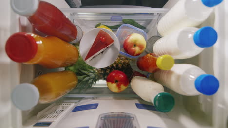 A-Woman's-Hand-Chooses-Between-An-Apple-And-A-Cake.-View-From-Inside-The-Refrigerator