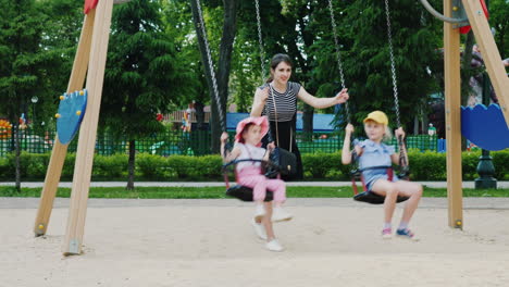 Young-Mother-Pushes-Two-Daughters-On-A-Swing-In-A-Park
